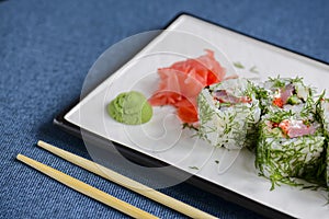 Salmon sushi rolls served on a white plate with ginger and wasabi and soy sauce in a restaurant table. Japanese cuisine.