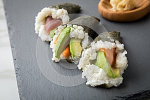 Salmon, tuna fish and Surimi avocado Temaki sushi with pickled ginger and wasabi on slate plate and marble background