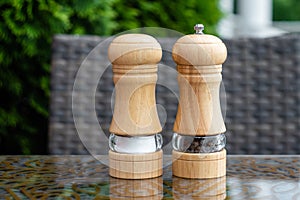 Salt and black pepper shakers in a summer cafe, a wooden pepper mill on a table in a restaurant. Spices, ingredients in cooking