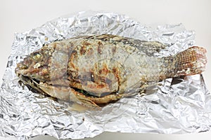 Salt-crusted grilled fish on foil white background isolated.