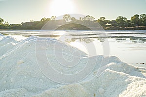 A salt crystals heap next to a pond full of salt after evaporation of ocean water at salines in Faro, Portugal