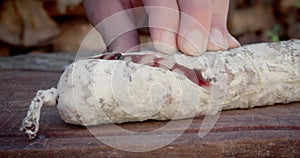 Salt-cured pork salami, sliced on a wooden board and a diffuse background of logs