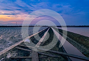 Salt farm in the morning with sunrise sky and clouds. Landscape of sea salt field in Thailand. Sea water in canal and soil pathway