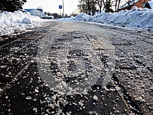 Salt grains on icy sidewalk surface in the winter