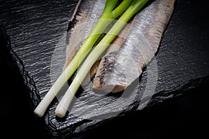 Salt Herring Fillets and Organic Green Onion Scallions arranged on black natural stone. Clupea harengus. Allium onion s