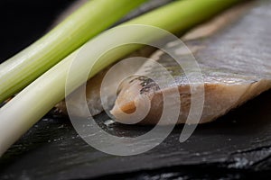 Salt Herring Fillets and Organic Green Onion Scallions arranged on black natural stone. Clupea harengus. Allium onion s