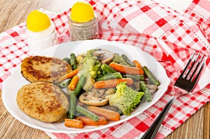 Salt and pepper, fried vegetable mix and cutlets in dish, fork on napkin on wooden table