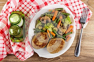 Salt and pepper, fried vegetable mix and cutlets in dish, fork on napkin on wooden table. Top view