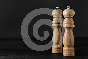 Salt and pepper shakers on black wooden table, closeup. Space for text