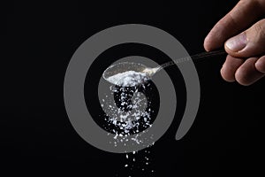 Salt is poured from a spoon on a black background. Excessive salt intake.