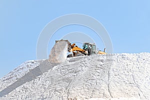 Salt production. Excavator working in a huge pile salt at saltworks. Marine salt produced by the evaporation of seawater