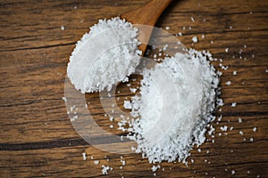 Salt in wooden spoon and heap of white salt on wood background