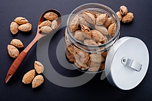 salted almonds in shell in glass jar and spoon on black slate