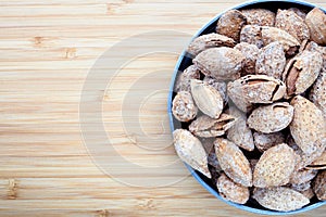 salted almonds in shell in metal plate on bamboo table top view