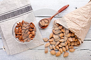 salted almonds in shell in paper bag on white wooden background