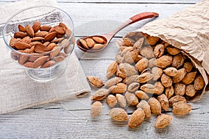 salted almonds in shell in paper bag on white wooden background