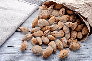 salted almonds in shell in paper bag on white wooden background