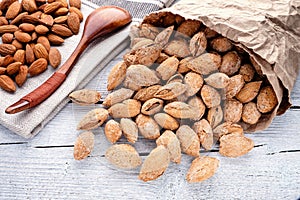 salted almonds in shell in paper bag on white wooden background