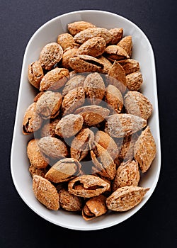 salted almonds in shell on white plate on black slate background