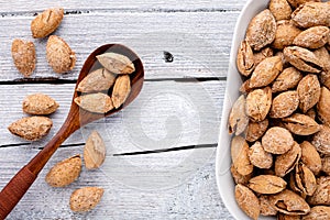 salted almonds in shell on white plate and spoon on white wood top view