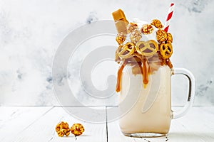 Salted caramel indulgent exreme milkshakes with brezel waffles, popcorn and whipped cream, Crazy freakshake food trend. Copy space photo