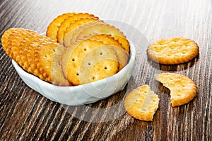 Salted crackers in bowl, broken cookie on wooden table