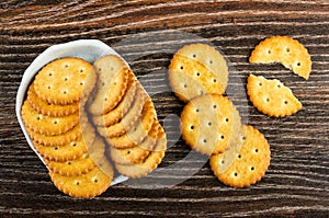 Salted crackers in bowl, broken cookie on wooden table. Top view