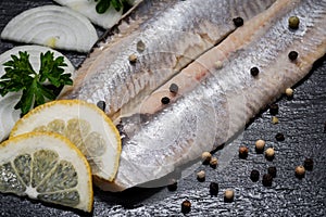 Salted Deboned Herring Fillets garnished with Yellow Onion, Lemon, Fresh Parsley and Peppercorns. Natural black stone .