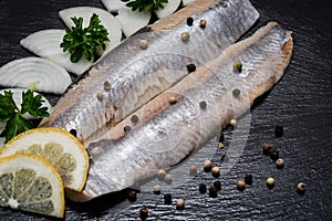 Salted Deboned Herring Fillets garnished with Yellow Onion, Lemon, Fresh Parsley and Peppercorns. Natural black stone .