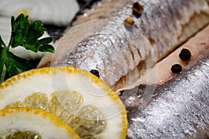 Salted Deboned Herring Fillets garnished with Yellow Onion, Lemon, Fresh Parsley and Peppercorns. Natural black stone .