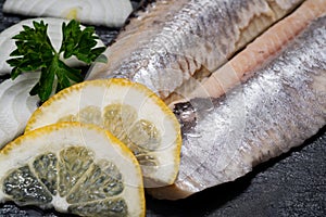 Salted Deboned Herring Fillets garnished with Yellow Onion, Lemon, Fresh Parsley and Peppercorns. Natural black stone .