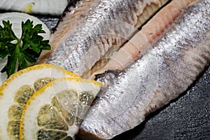 Salted Deboned Herring Fillets garnished with Yellow Onion, Lemon, Fresh Parsley and Peppercorns. Natural black stone .