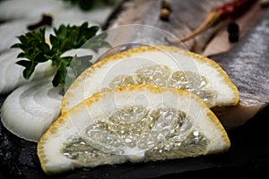 Salted Deboned Herring Fillets garnished with Yellow Onion, Lemon, Fresh Parsley and Peppercorns. Natural black stone .