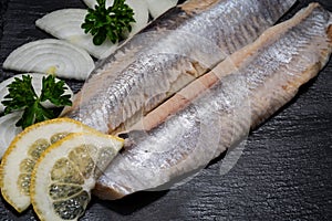 Salted Deboned Herring Fillets garnished with Yellow Onion, Lemon, Fresh Parsley and Peppercorns. Natural black stone .