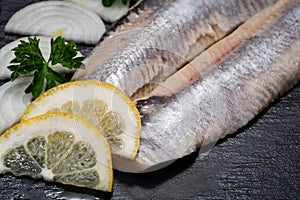 Salted Deboned Herring Fillets garnished with Yellow Onion, Lemon, Fresh Parsley and Peppercorns. Natural black stone .