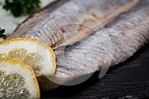 Salted Deboned Herring Fillets garnished with Yellow Onion, Lemon, Fresh Parsley and Peppercorns. Natural black stone .