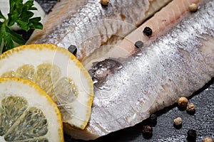 Salted Deboned Herring Fillets garnished with Yellow Onion, Lemon, Fresh Parsley and Peppercorns. Natural black stone .