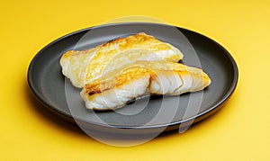 Salted and dried cod served on a sleek charcoal plate with a deep yellow backdrop adding a vibrant contrast photo