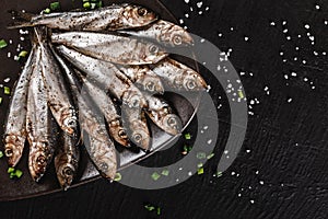 Salted fishes sprat marinated with spices, salt on plate over dark stone background. Mediterranean food, appetizer, seafood, top