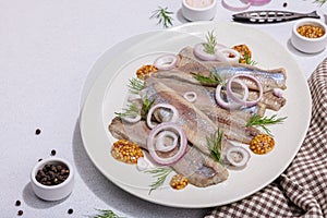 Salted herring with dijon mustard, dill and red onion rings on white stone background