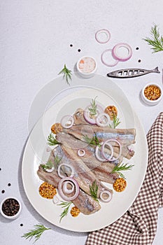Salted herring with dijon mustard, dill and red onion rings on white stone background