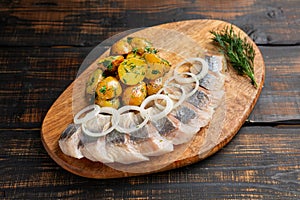 Salted herring with spice, herbs and onion on dark wooden background