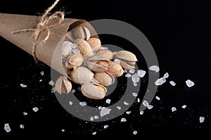 Salted pistachios in craft paper, in a craft bag with large grains of salt on a black background