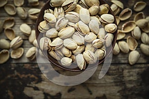 Salted pistachios in a wooden bowl on wooden rustic background, top view