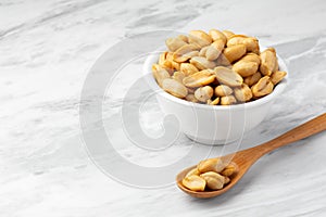 Salted roasted peanuts in white bowl with wood spoon on marble table