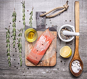 Salted salmon fillet on a cutting board with rosemary, pepper, oil, lemon and a wooden spoon salt on wooden rustic backgroun