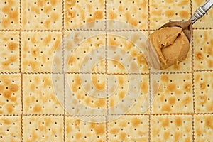 Saltine crackers background with spoon full of peanut butter photo