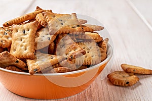 Saltine crackers in an orange bowl on a white wood table. Deep plate full of salty crackers with black and white sesame seeds