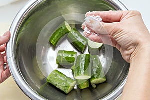 Salting fresh green sliced cucumber in the kitchen