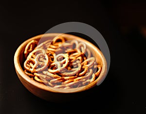 Salty beer snack pretzels with salt in a wooden bowl on a black background.